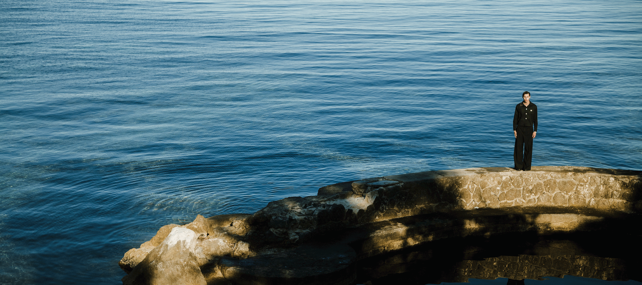 Person in dunkler Kleidung steht am Meer. Daneben ein Button mit der aufschrift - New Summer Collection